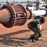 A soldier crossing under a pipeline.