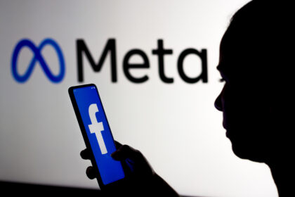 March 16, 2022, Brazil. In this photo illustration, a woman holds a smartphone with the Facebook logo displayed on the screen with the Meta Platforms logo displayed in the background