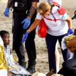 A police officer holds a migrant's baby, while she rests on the sand after arriving in a fiber boat at Las Burras beach in San Agustin, on the island of Gran Canaria, Spain, July 19, 2024. REUTERS/Borja Suarez