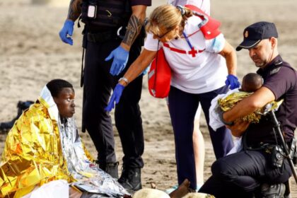 A police officer holds a migrant's baby, while she rests on the sand after arriving in a fiber boat at Las Burras beach in San Agustin, on the island of Gran Canaria, Spain, July 19, 2024. REUTERS/Borja Suarez