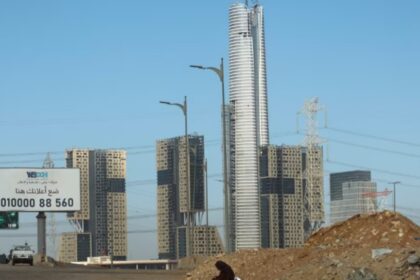 A woman sits on the road next to the construction site of the Iconic Tower skyscraper in the Central Business District (CBD), which is being built by China State Construction Engineering Corp (CSCEC) in the New Administrative Capital (NAC) east of Cairo, Egypt January 15, 2023. REUTERS/
